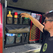 Load image into Gallery viewer, Person organising items in a compartment of a vehicle, with a focus on camping gear and supplies.