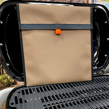 Load image into Gallery viewer, Brown canvas bag with black trim and orange tag on a BBQ