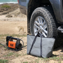 Load image into Gallery viewer, Car tyre with a portable air compressor and tire inflator bag on a beach.