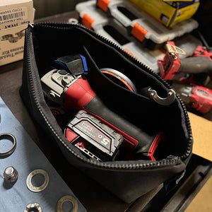 Black tool pouch with angle grinder and battery on a workshop bench.