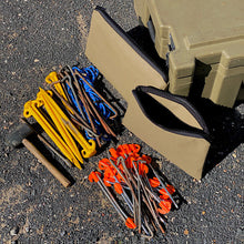 Load image into Gallery viewer, Collection of tent stakes, a hammer, and a green carrying case on a gravel surface.