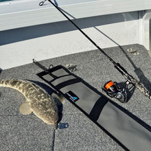 Load image into Gallery viewer, A fishing rod with a spinning reel lies on a gray boat deck next to a caught fish and a gray canvas rod cover 