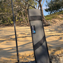 Load image into Gallery viewer, A black and gray rod cover standing upright on a sandy beach with trees in the background.