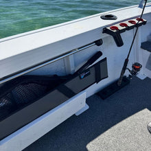 Load image into Gallery viewer, A black and gray boat storage rack mounted on the side of a white boat, holding a fishing rod and net, with ocean water visible in the background.