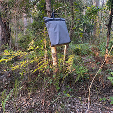 Load image into Gallery viewer, Canvas trash bag hanging from a tree in a forest setting to protect from wildlife