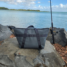 Load image into Gallery viewer, Grey canvas fishing bag on rocks with a fishing rod by the water