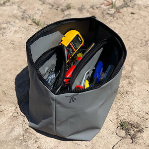 Grey canvas bag with tools inside sitting on sand